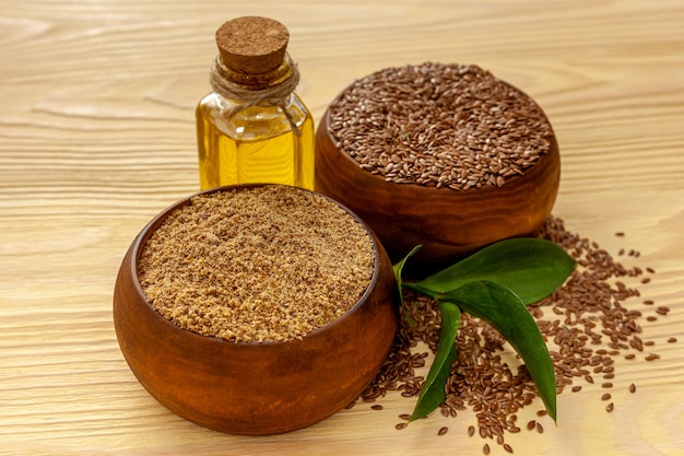 Flaxseeds in a spoon and bowl with a bottle of flaxseed oil and flaxseed flour
