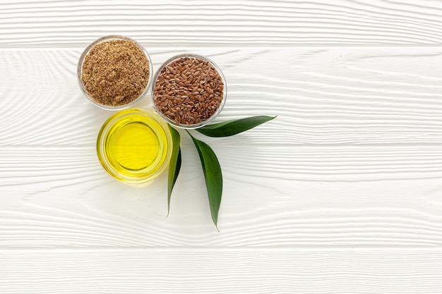 Flaxseeds in a spoon and bowl with a bottle of flaxseed oil and flaxseed flour