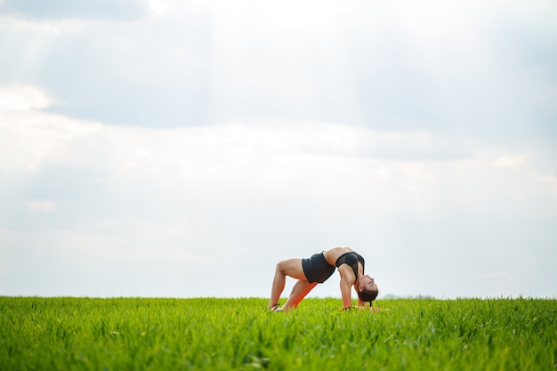 Flexible girl, acrobat, gymnastic bridge, handstand, graceful woman. In nature, performs beautiful poses for flexibility, a sports model on a blue sky background.