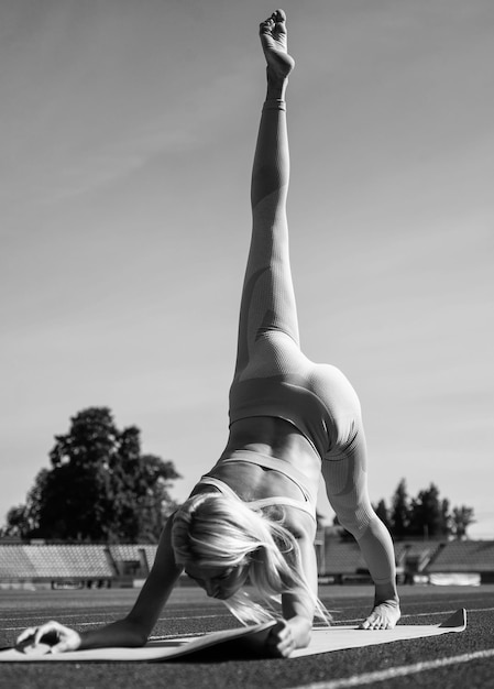 Flexible woman stretching on stadium in sportswear pilates