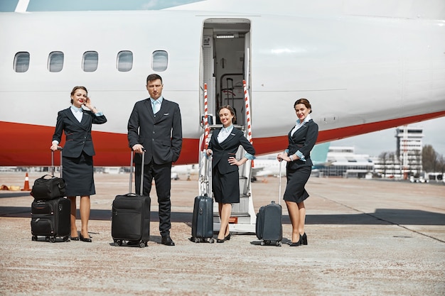 Flight attendant and stewardesses standing on runway near airplane jet. Modern passenger plane. Man and women with luggage wear uniform. Teamwork. Civil commercial aviation. Air travel concept