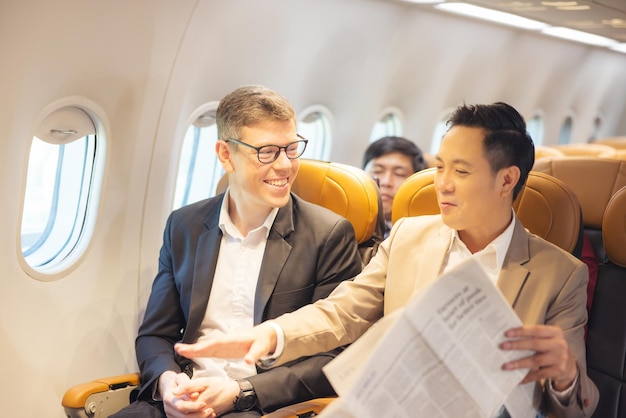 During a flight a businessman in formal attire and glasses works with a friend near the window business travel concept