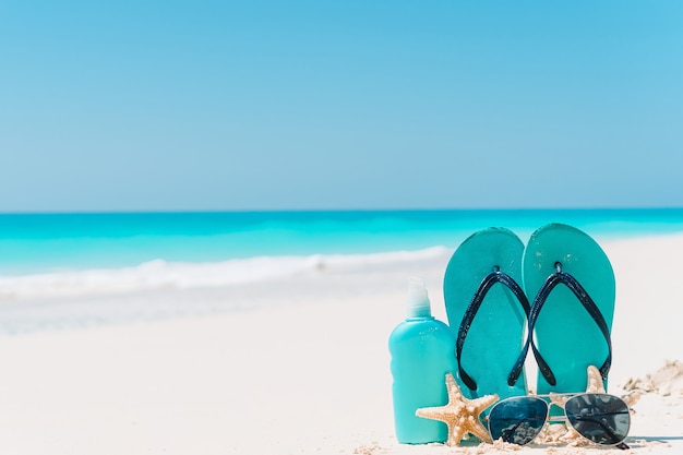 Flip flop, suncream bottles, goggles, starfish and sunglasses on white sand beach background ocean