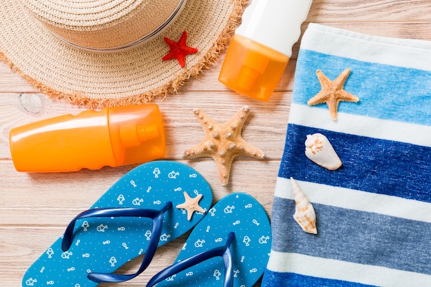 Flip flops, straw hat, starfish, sunscreen bottle, body lotion spray on wooden background top view . flat lay summer beach sea accessories background, holiday concept.