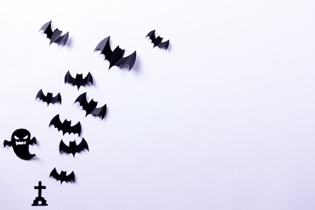 Flock of black paper bats and ghost on white surface