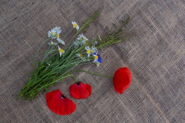 Floral arrangement of red poppies daisies cornflowers and wildflowers on a background of burlap