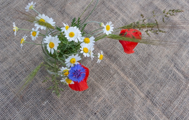 Floral arrangement of red poppies daisies cornflowers and wildflowers on a background of burlap