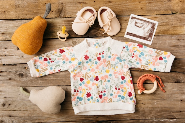 Floral baby clothing with shoes; pacifier; ultrasound picture and stuffed toy on wooden table