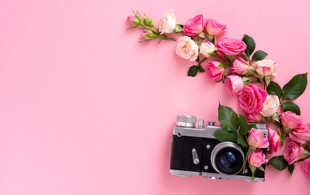 Floral composition with a wreath of pink roses and retro camera on pink background. Valentine's Day background. Flat lay, top view.