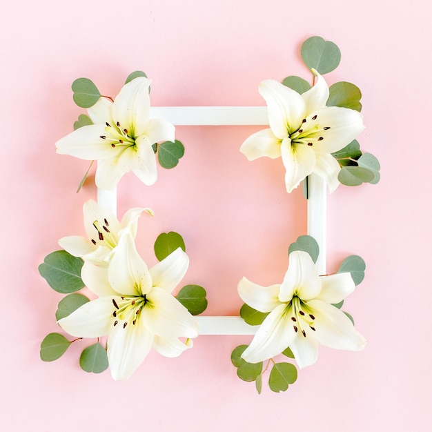 Floral frame made of white lilies and eucalyptus leaves on pink background flat lay top view floral