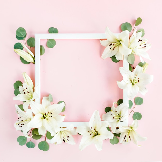 Floral frame made of white lilies and eucalyptus leaves on pink background flat lay top view floral