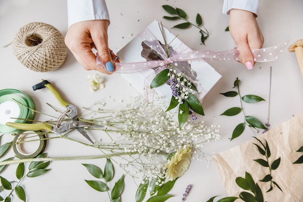 A florist decorates a gift box with flowers and a ribbon