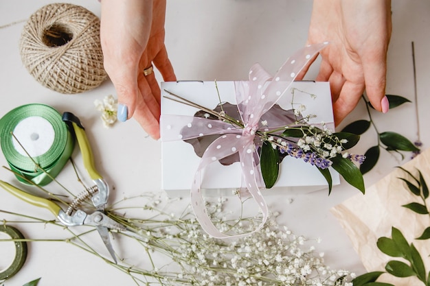 A florist decorates a gift box with flowers and a ribbon