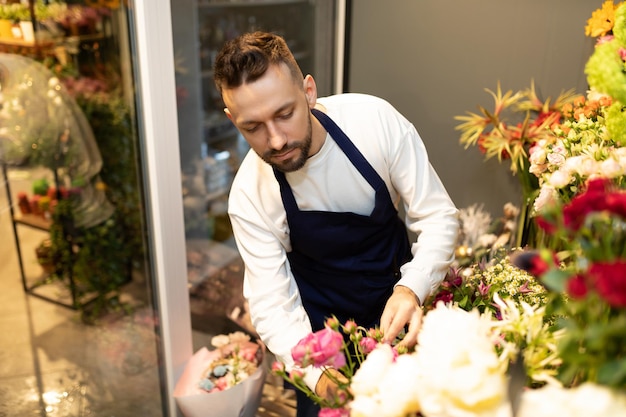 A florist in a flower shop collects a bouquet of freshly cut roses in a special florist refrigerator