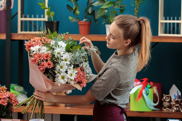 Florist makes a bouquet. A young adult girl holds a large bouquet of multi-colored chrysanthemums in her hands and checks it.