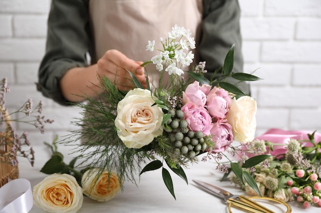 Florist making beautiful bouquet at white table closeup