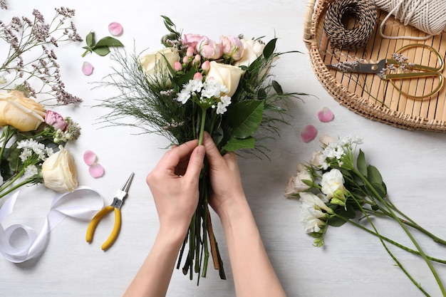 Florist making beautiful bouquet with roses at white table top view