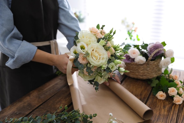 Florist making beautiful wedding bouquet at wooden table closeup