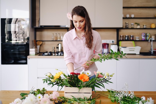 Florist at work pretty young brunette woman making fashion modern composition of different flowers at home