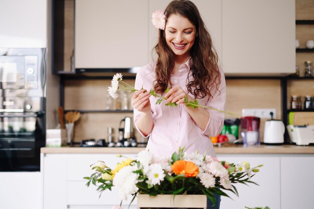 Florist at work pretty young brunette woman making fashion modern composition of different flowers at home