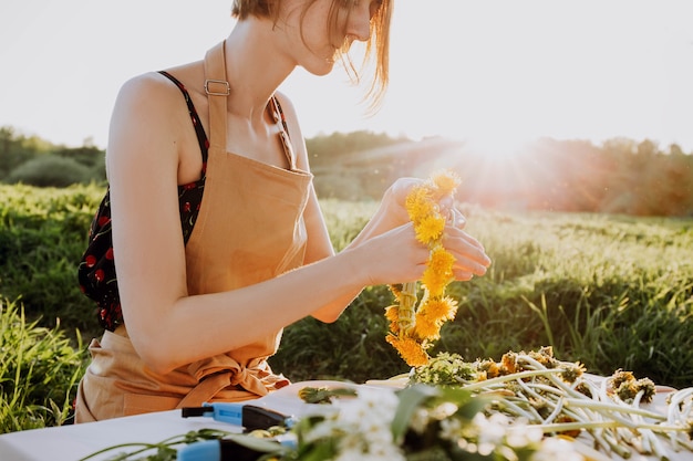 Florist workshop. Pretty woman making wreath from dandelions. Romantic background of florist at work.