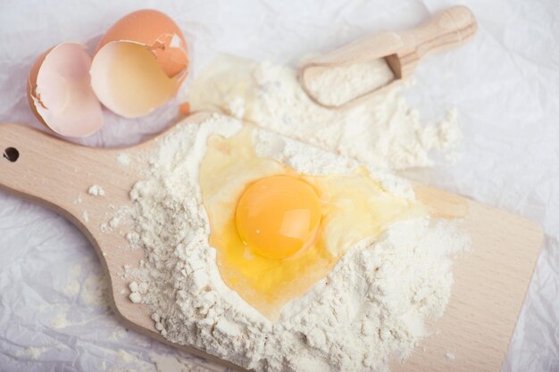 Photo flour and egg yolk on wooden cutting board close up photo