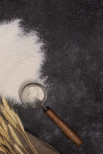 Photo flour in a plate with a flour scoop. the texture of the black background. ears of wheat