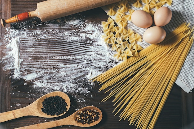 Flour spread and pasta on wooden background