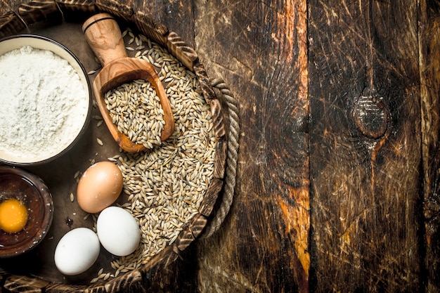 Flour with wheat grains on an old tray. On a wooden background.