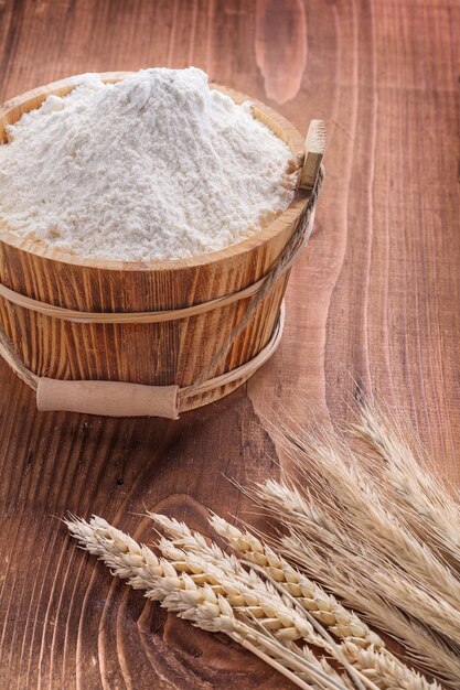 Flour in wooden bucket and ears of wheat on vintage board food and drink concept