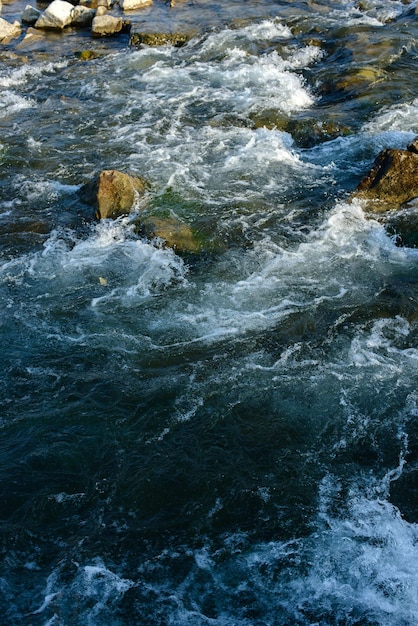 Flow for a stormy river among the rocks in the autumn park on a warm day