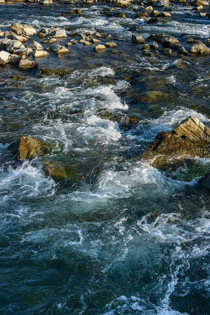 Flow for a stormy river among the rocks in the autumn park on a warm day