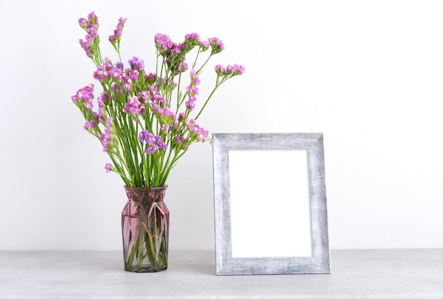 Flower bouquet in glass vase and blank grey vintage wooden frame on table background