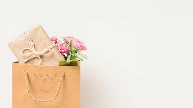 Flower bouquet and wrapped gift box in paper bag with hand drawn face isolated on white background