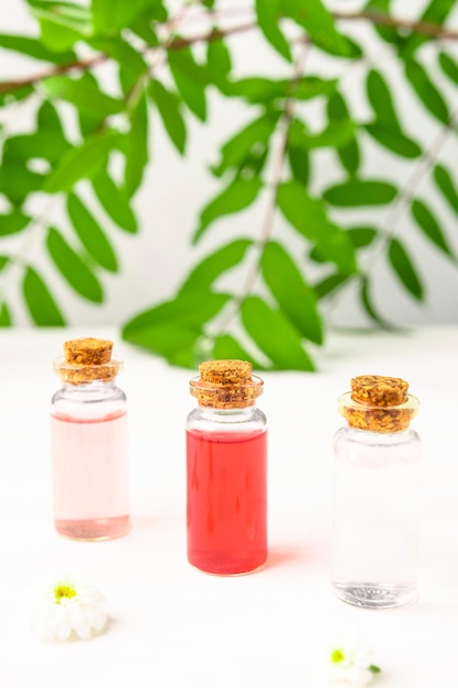 Flower extracts of a garden rose in glass containers on a white wooden table with juicy greens