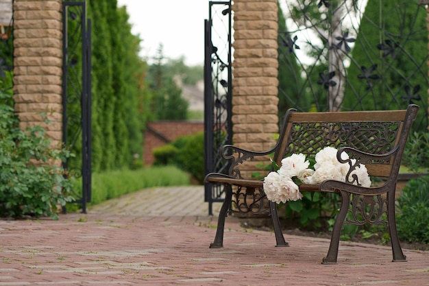 Flower garden and vintage bench A bouquet of peonies on a bench near a private house