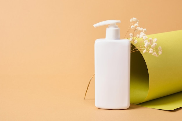 Flower and mock up blank white bottle with dispenser for cosmetics on the background of a roll of green paper texture