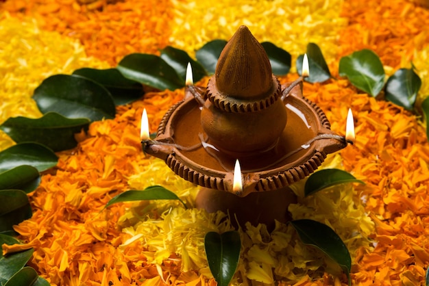 Photo flower rangoli for diwali or pongal made using marigold or zendu flowers and red rose petals over white background with clay oil lamp in the middle, selective focus