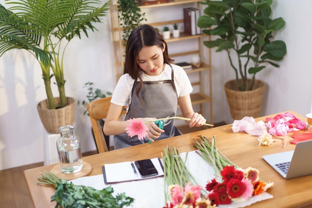 Flower shop concept Female florist cutting gerbera with scissor to prepare for making flower vase