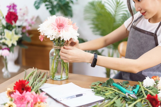 Flower shop concept Female florist is decorating colorful flowers vase by hemp rope in bow shape