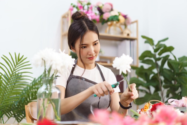 Flower shop concept Female florist trim leaf of chrysanthemums with scissor for arranging in vase