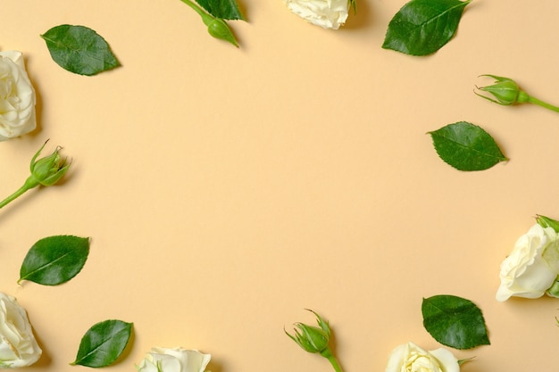 Flowers composition. Frame made of roses flowers and green leaves on pastel yellow background.