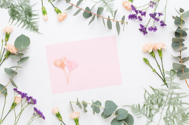 Flowers composition. Paper blank, carnation flowers, eucalyptus branches on pastel  background. Flat lay, top view, copy space