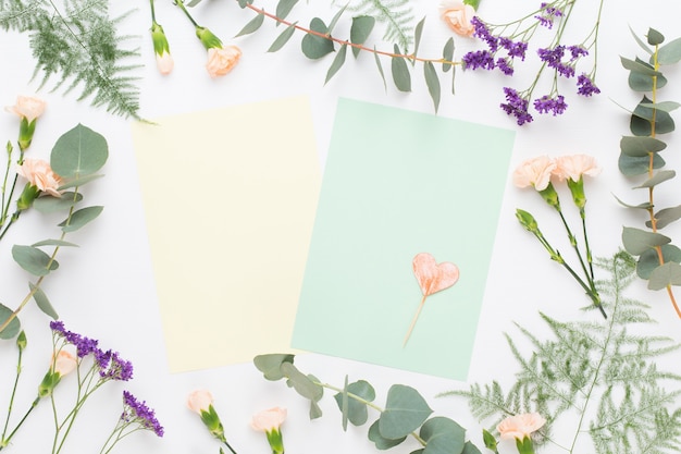 Flowers composition. Paper blank, carnation flowers, eucalyptus branches on pastel  background. Flat lay, top view.