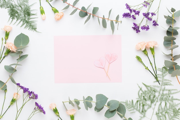 Flowers composition. Paper blank, carnation flowers, eucalyptus branches on pastel  background. Flat lay, top view.