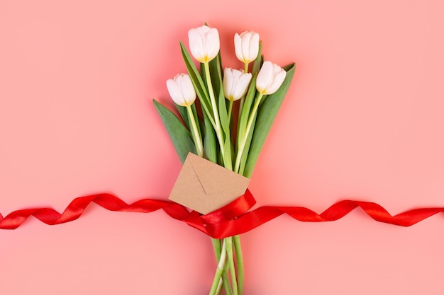 Flowers flatlay A beautiful bouquet tied with a red ribbon and an envelope on pink background