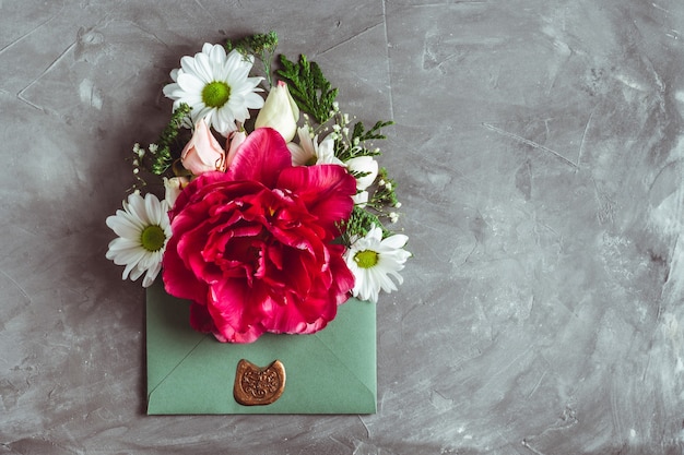 Flowers in green envelope on gray concrete background. Large tulip, roses and chrysanthemums. Flat lay, copy space