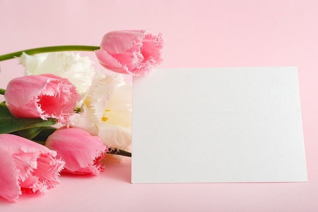 Photo flowers mock up congratulation. congratulations card in bouquet of pink tulips on pink background. white blank card with space for text, frame mockup. spring festive flower concept, gift card.