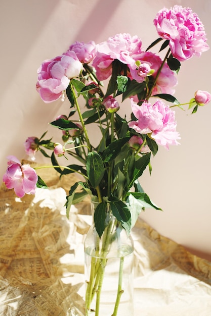 Fluffy bouquet of pink peonies flowers in sunlight on wrinkled craft paper background Valentines day and Womans day background