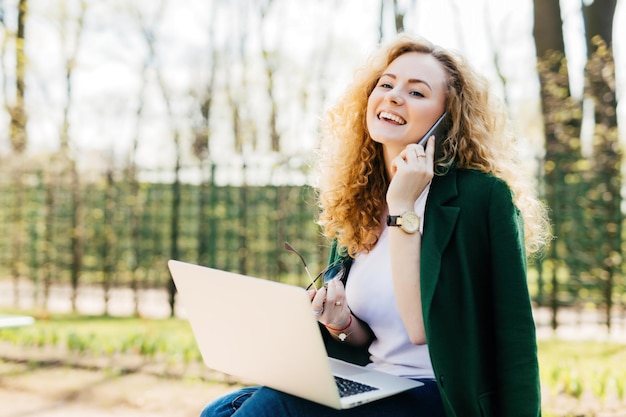 Fluffyhaired beauty holding smartphone and sunglasses excitedly talking to best friend Laptop in use